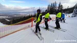 Trzej policjanci na nartach stojący na stoku, w tle góry.