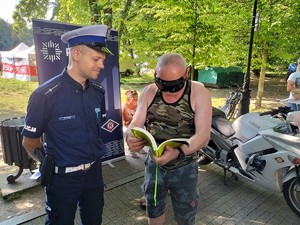 Zdjęcie kolorowe: widoczny umundurowany policjant ruchu drogowego wraz z mężczyzną w alkogoglach.
