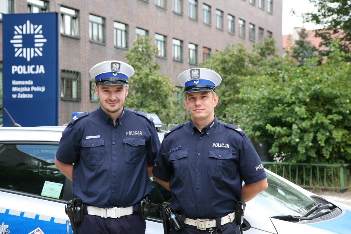 na zdjęciu dwóch umundurowanych policjantów, w tle radiowóz i budynek komendy policji w zabrzu
