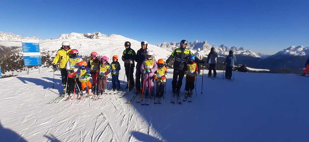 Trzech umundurowanych policjantów z grupą dzieci na stoku narciarskim