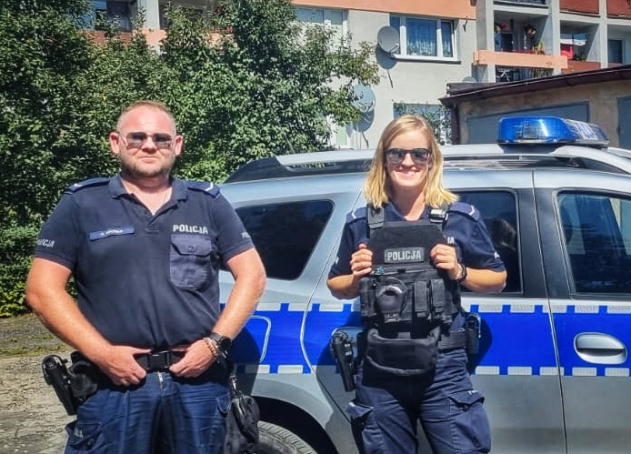 policjant i policjantka stoją przed radiowozem