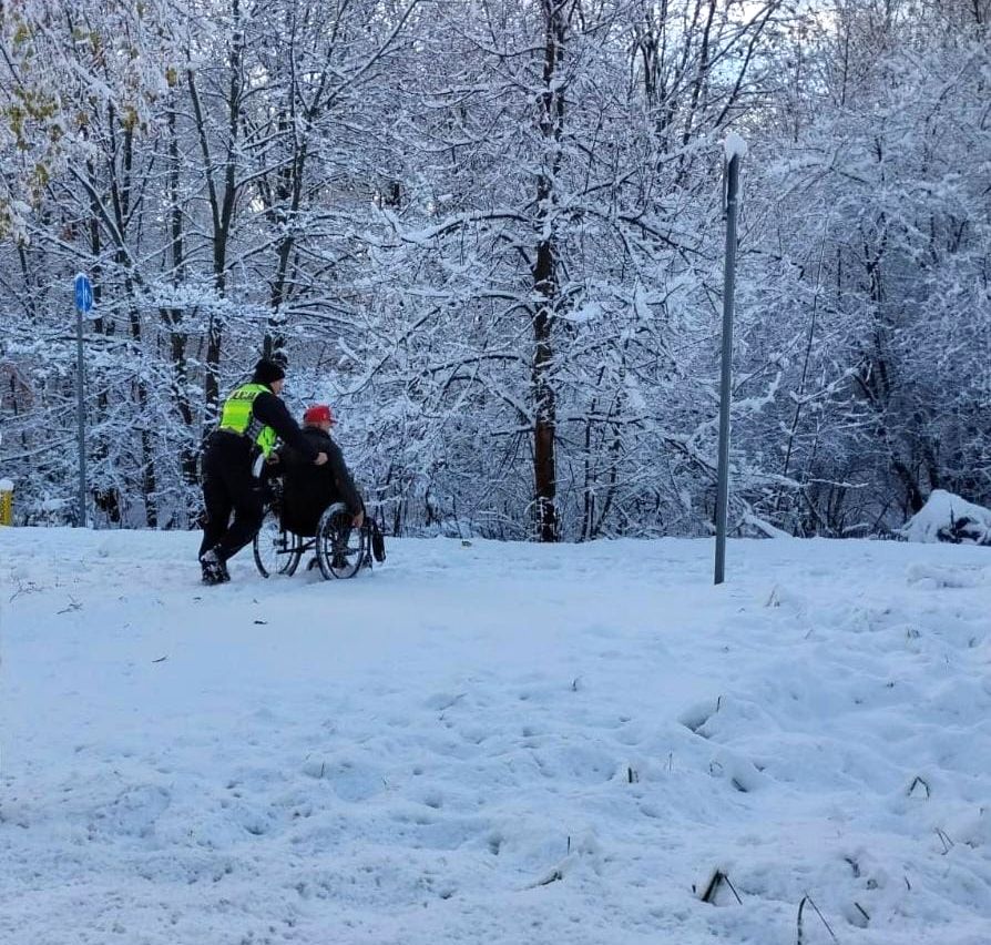 Na zdjęciu policjant pomaga niepełnosprawnemu mężczyźnie na wózku inwalidzkim.