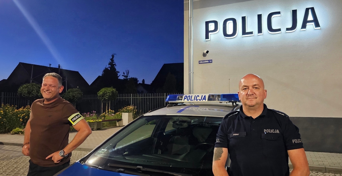 Dwaj policjanci stoją przy radiowozie.