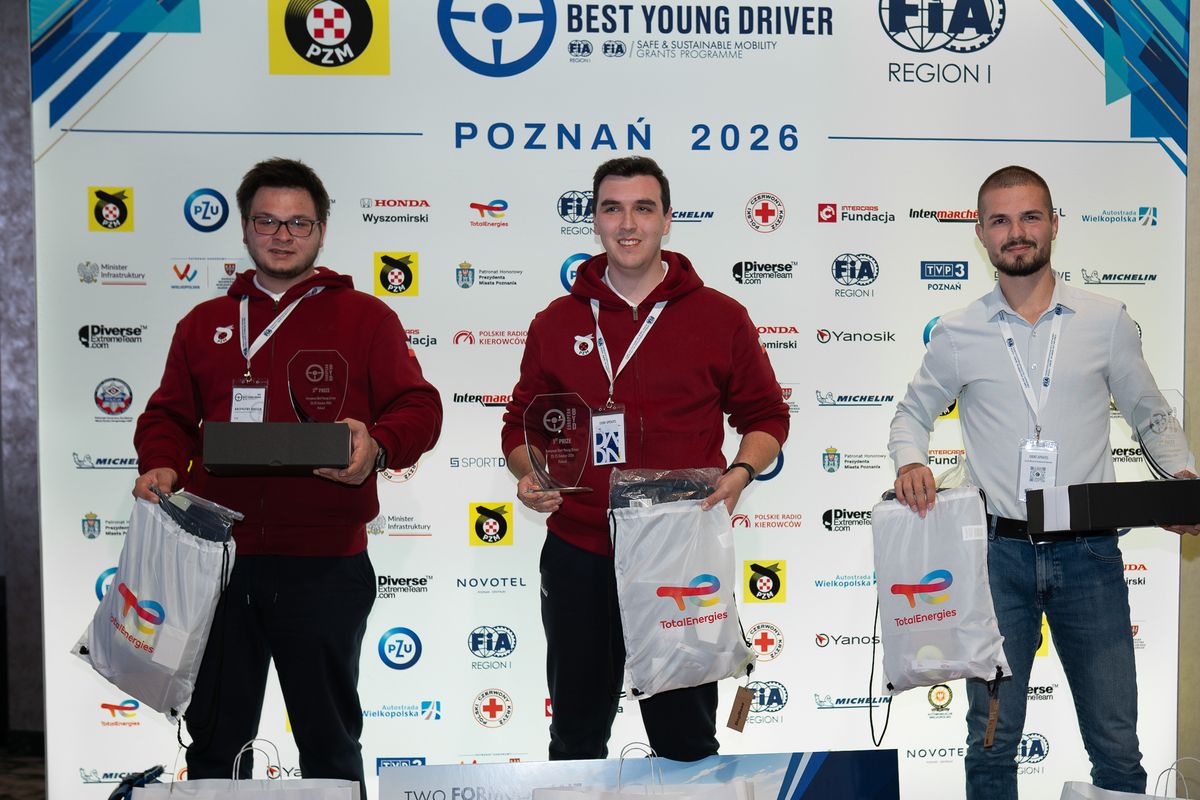 Trzej zwycięzcy mężczyxni na scenie z medalami na szyi i nagrodami.