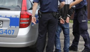 Policjanci z KPP Oświęcim prowadzą do policyjnego radiowozu zatrzymanego włamywacza