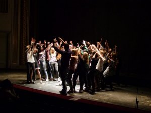 przedstawienie – młodzież na scenie stoi w kręgu, z uniesionymi rękami