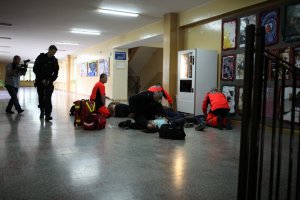 ratownicy medyczni i policjanci udzielają pomocy rannym na korytarzu szkoły