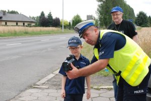 policjant ruchu drogowego pokazuje chłopcu jak działa laserowy miernik prędkości