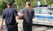 Policjant prowadzi jednego z zatrzymanych za kradzieże z włamaniem