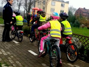 Dzieci na rowerach w towarzystwie policjantki, w kamizelkach odblaskowych