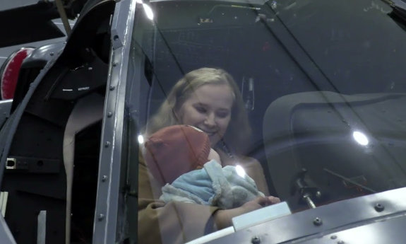 Uśmiechnięta kobieta z dzieckiem na ręku siedzi w kabinie śmigłowca.