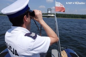 policjant na łodzi obeserwujący jezioro przez lornetkę
