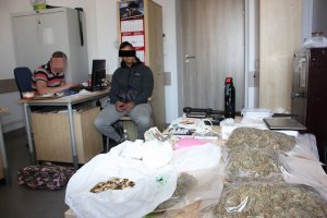 policjant przesłuchuje zatrzymanego na stole zabezpieczone narkotyki i pieniądze