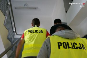 Zatrzymany mężczyzna odprowadzany na schodach przez policjantów