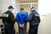zatrzymany mężczyzna w kajdankach prowadzony przez policjantów do celi