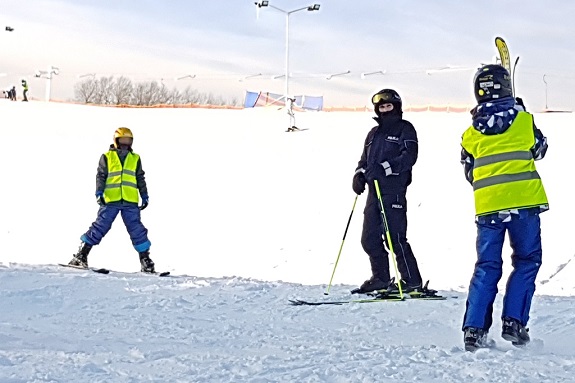 na stoku narciarskim stoją dzieci z nartami oraz policjant na nartach