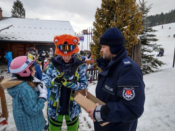 Policjant rozdaje ulotki dzieciom na stoku narciarskim