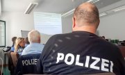 Grupa osób, w tym niemieccy policjanci siedzą na sali.
