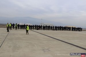 policjanci stoją w szeregu na płycie lotniska