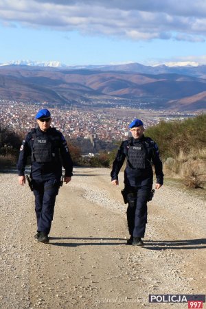 dwaj policjanci w błękitnych beretach idą drogą, w kierunku aparatu, gdzieś poza miastem