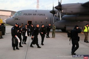 Płyta lotniska, w tle samolot z napisem Polish Air Force, przed nim uśmiechnięci policjanci, wysiadają z samolotu