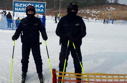 Policjanci stoją na nartach na stoku narciarskim.