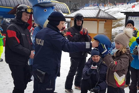 policjanci rozdają ulotki, informatory i kaski narciarskie na  stoku w ramach prowadzonych działań profilaktycznych