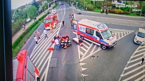 Miejsce wypadku drogowego, widzimy udzielających pomocy rannemu motocykliści. Widać pojazdy pogotowia i straży pożarnej