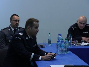 Trzech mężczyzn w mundurach galowych rozmawiają siedząc przy stole.