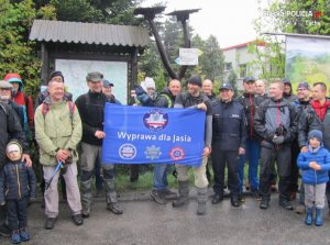 Obrazek przedstawia kilkanaście osób stojących na mecie przy dworcu Ustroń Zdrój, trzymają niebieską flagę z napisem &quot;Wyprawa dla Jasia&quot;