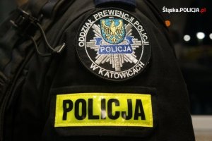emblemat Oddziałów Prewencji Policji w Katowicach oraz napis Policja na ramieniu umundurowanego policjanta