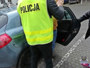 Na zdjęciu policjanci wprowadzają zatrzymanego mężczyznę do radiowozu.