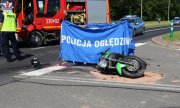 motocykl leżący na skrzyżowaniu po wypadku, parawan z napisem policja w tle widać wóz strażacki