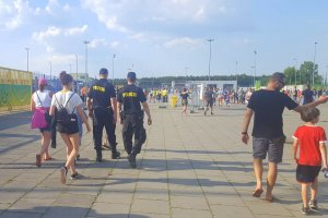 dwaj policjanci patrolują teren przy stadionie, a obok przechodzą kibice udający się na mecz