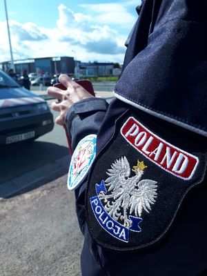 Na ramieniu munduru policyjnego widoczny emblemat policyjny z orłem oraz  napisem „POLAND”.