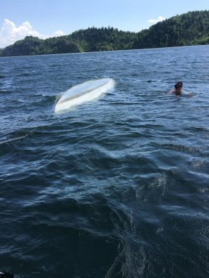 wywrócona łódź na jeziorze i człowiek w wodzie
