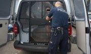 policjant zamyka drzwi radiowozu policyjnego, w którym siedzi zatrzymany mężczyzna