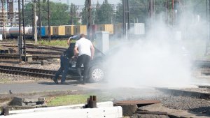 samochód stojący na torach z otwartą maską z silnika leci dym, przy samochodzie dwaj mężczyźni