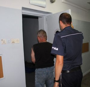 kolorowe zdjęcie przedstawiające umundurowanego policjanta osadzającego  zatrzymanego w pomieszczeniu dla osób zatrzymanych