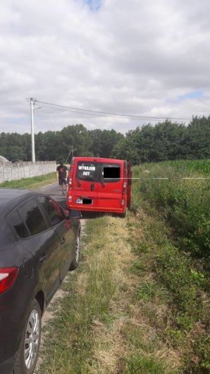 na poboczu drogi stoi czerwony bus z napisem wynajem aut, po lewej stronie widać bok samochodu w kolorze czarnym