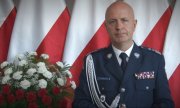 Komendant Główny Policji na tle biało-czerwonych flag.