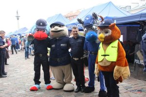 wspólne zdjęcie policjanta i kilku policyjnych maskotek, w tle stoiska policyjne