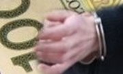 Na zdjęciu widoczny jest ręka w kajdankach, na tle banknotu.