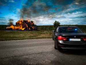 policyjny czarny radiowóz BMW oraz palące się w oddali bele słomy