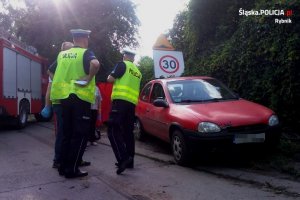 2 policjantów drogówki wykonuje czynności na miejscu wypadku. obok czerwony opel corsa