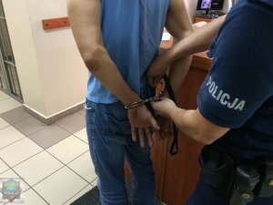 Zatrzymany mężczyzna z kajdankami zapiętymi na ręce, prowadzony przez policjanta