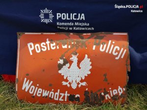 Na zdjęciu znajduje się szyld komisariatu Policji Województwa Śląskiego z tylu logo KMP Katowice
