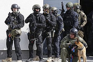 grupa sześciu policjantów uzbrojonych oraz pies służbowy