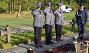 trzej policjanci salutując przed grobami oddają hołd poległym w Palmirach