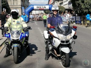 dwaj policjanci na motocyklach - z tyłu zawodnicy na starcie biegu